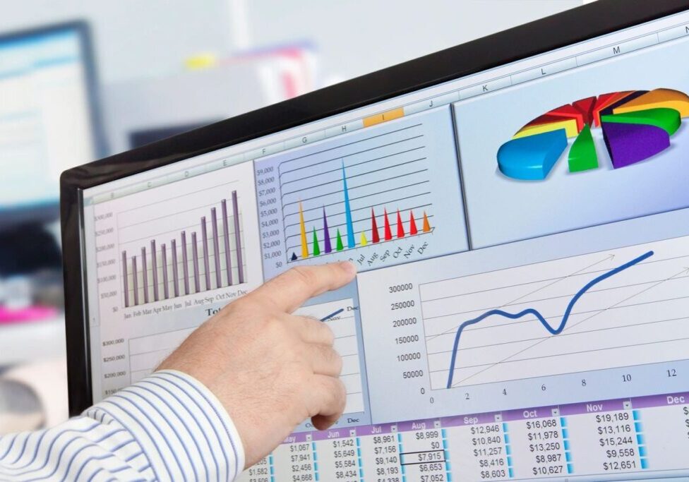 A person pointing to a computer screen with graphs on it.